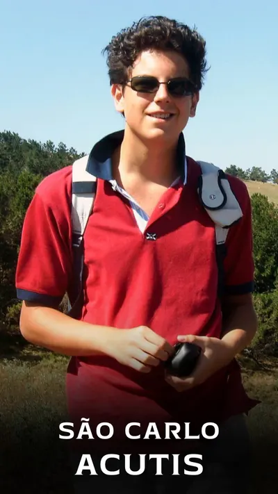 Foto de Carlo Acutis adolescente, de óculos escuros e polo vermelha, sorrindo ao ar livre com mochila.